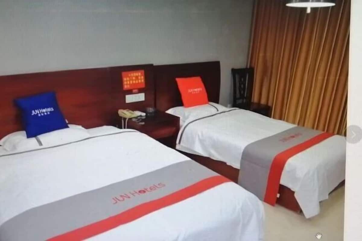 Two twin beds with white bedding and red accents, a wooden headboard, a nightstand with a red lamp, and a curtain in the background.