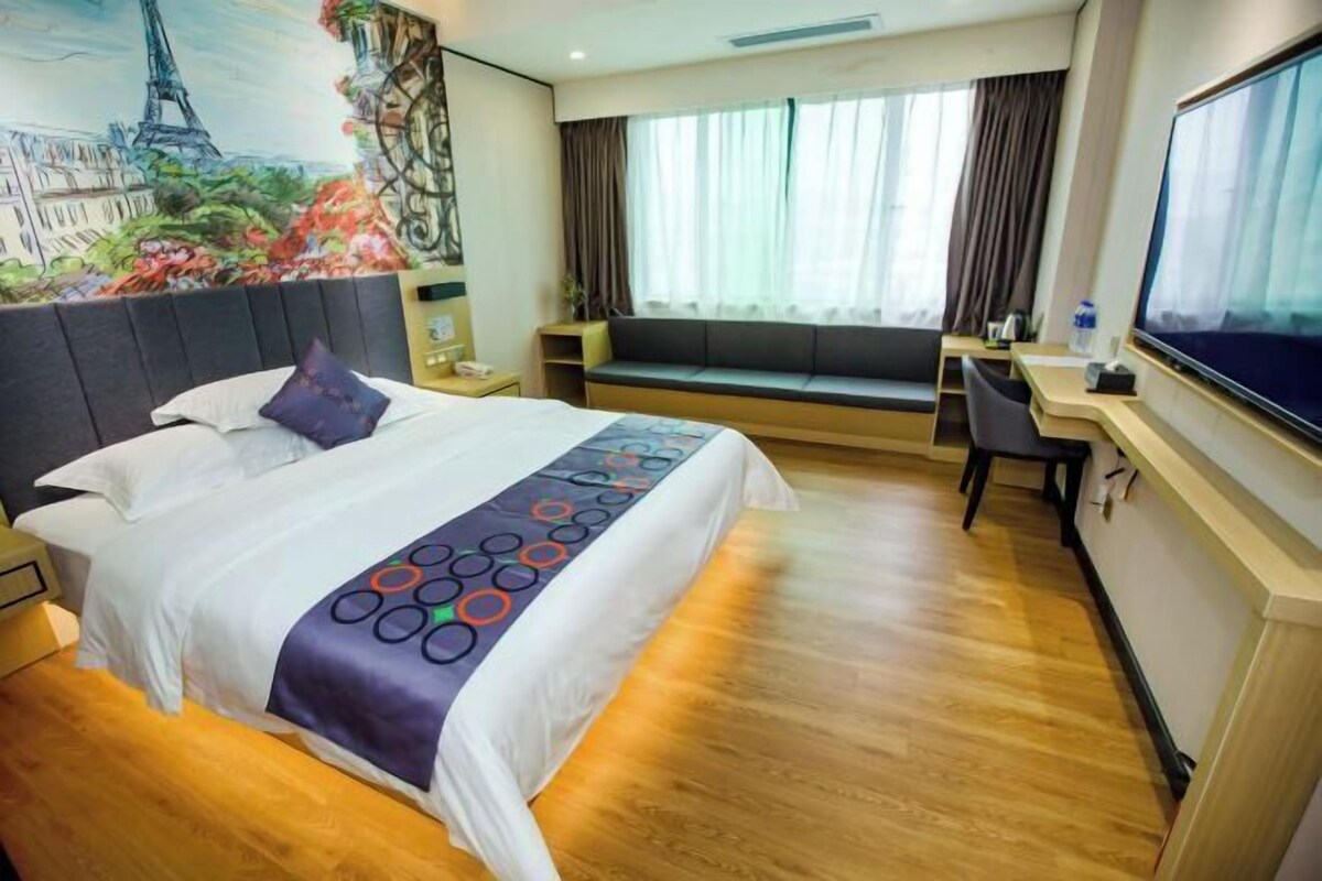 A hotel room with a bed, a desk, a television, a window with curtains, and a mural of the Eiffel Tower.
