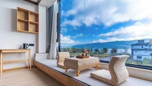 A modern room with a large window, a wooden table, two wicker chairs, and a view of mountains.