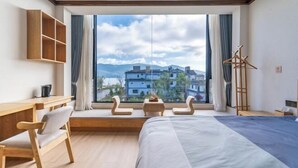 A modern hotel room with a large window, a bed, a desk, and a chair.