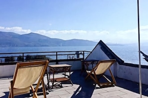 A terrace with two wooden chairs and a table, overlooking a body of water and distant mountains. - Dali Liwan Seaview Inn (Dali City)