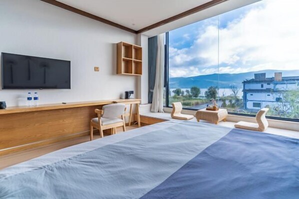 Ein modernes Hotelzimmer mit einem großen Bett, einem an der Wand montierten Fernseher, einem Holztisch und Bergblick durch große Fenster.
