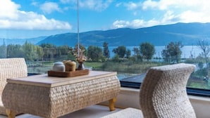 A room with a view of mountains and a lake, featuring a woven table and two chairs.