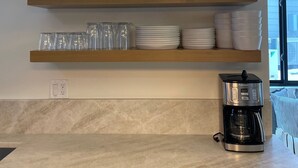 A kitchen with a coffee maker, shelves with cups and glasses, and a potted plant. - Creekside 3B/3B Townhome - 1 Block to Ski Lift! (Park City)