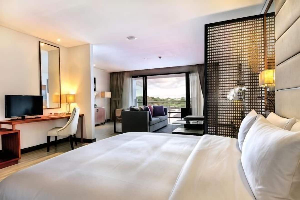 A hotel room with a large bed, a desk with a TV, a sofa, and a view of the outdoors.