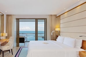 A hotel room with a bed, a desk, a chair, and a view of the sea through large glass doors. - LV8 Resort Hotel Bali (Bali)
