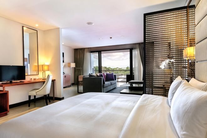 A hotel room with a large bed, a desk with a chair, a sofa, a TV, and a balcony with a view.