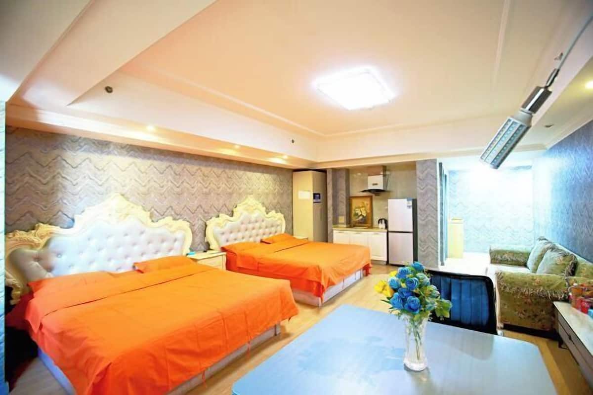A hotel room with two beds, a dining table, a small kitchen area, and a sofa.
