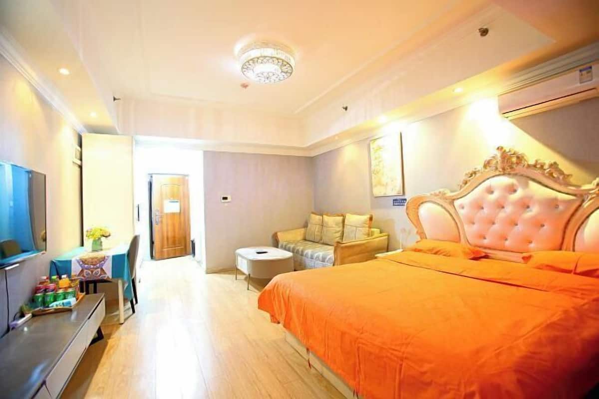 A hotel room with a large bed, a television, a desk with a chair, and a small round table.