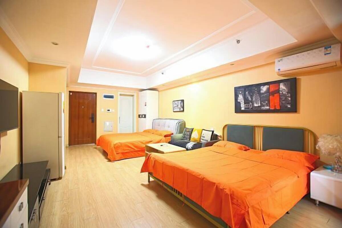 A hotel room with two beds, a desk, a chair, a TV, and an air conditioning unit.