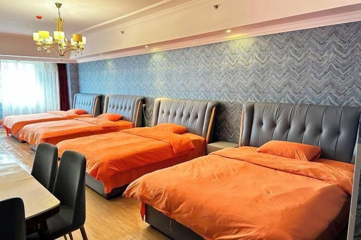 A hotel room with four beds, a chandelier, a herringbone-patterned wall, and a wooden floor.