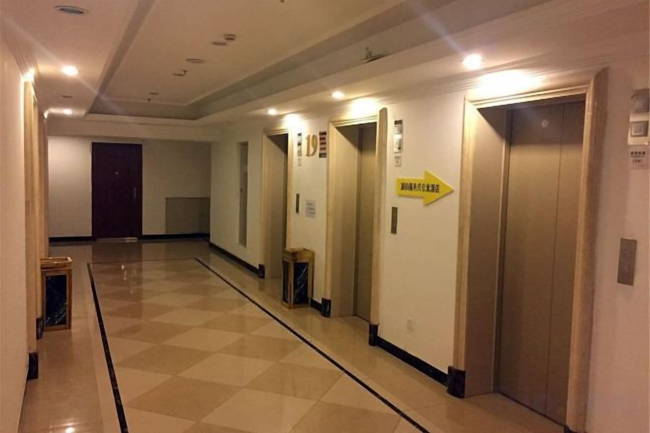 A hotel corridor with multiple doors, including an elevator and a trash bin.