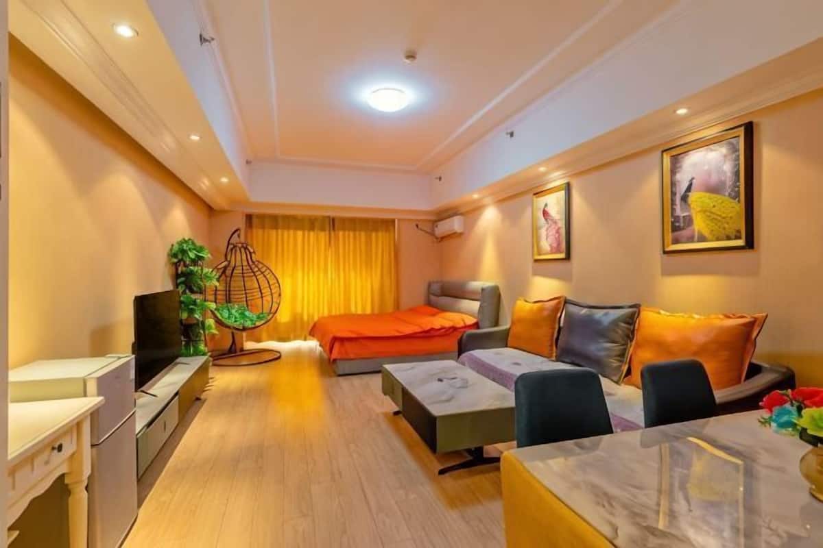 A hotel room with a bed, sofa, dining table, TV, and a plant.
