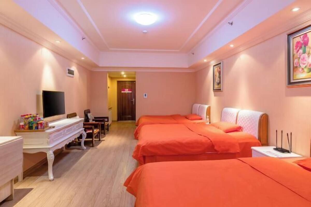 A hotel room with three beds, a desk with a flat-screen TV, a dresser, and a painting on the wall.