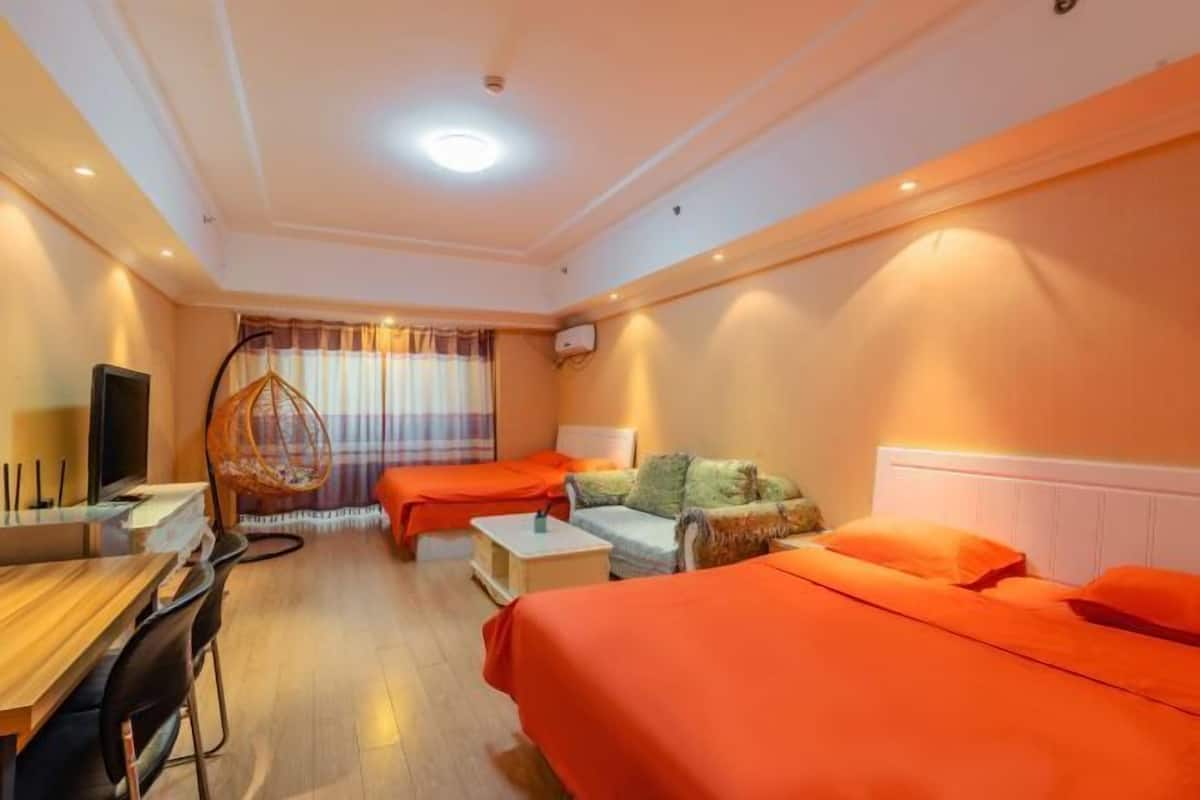 A hotel room with two beds, a desk, a chair, a hanging chair, and a television.
