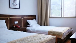 A hotel room with two beds, a window with curtains, a framed picture on the wall, and a bedside table with a red object.