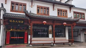 A traditional Chinese building with a tiled roof and wooden beams. There is a sign with Chinese characters and a red lantern hanging above the entrance.