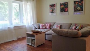 A living room with a sofa, a small side table, and a window with curtains. There are three framed pictures on the wall. - Relaxing Birdsong Bungalow (Port Dover)