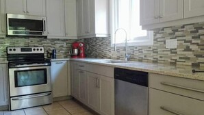 A kitchen with stainless steel appliances, a red coffee maker, and a tiled backsplash. - Relaxing Birdsong Bungalow (Port Dover)