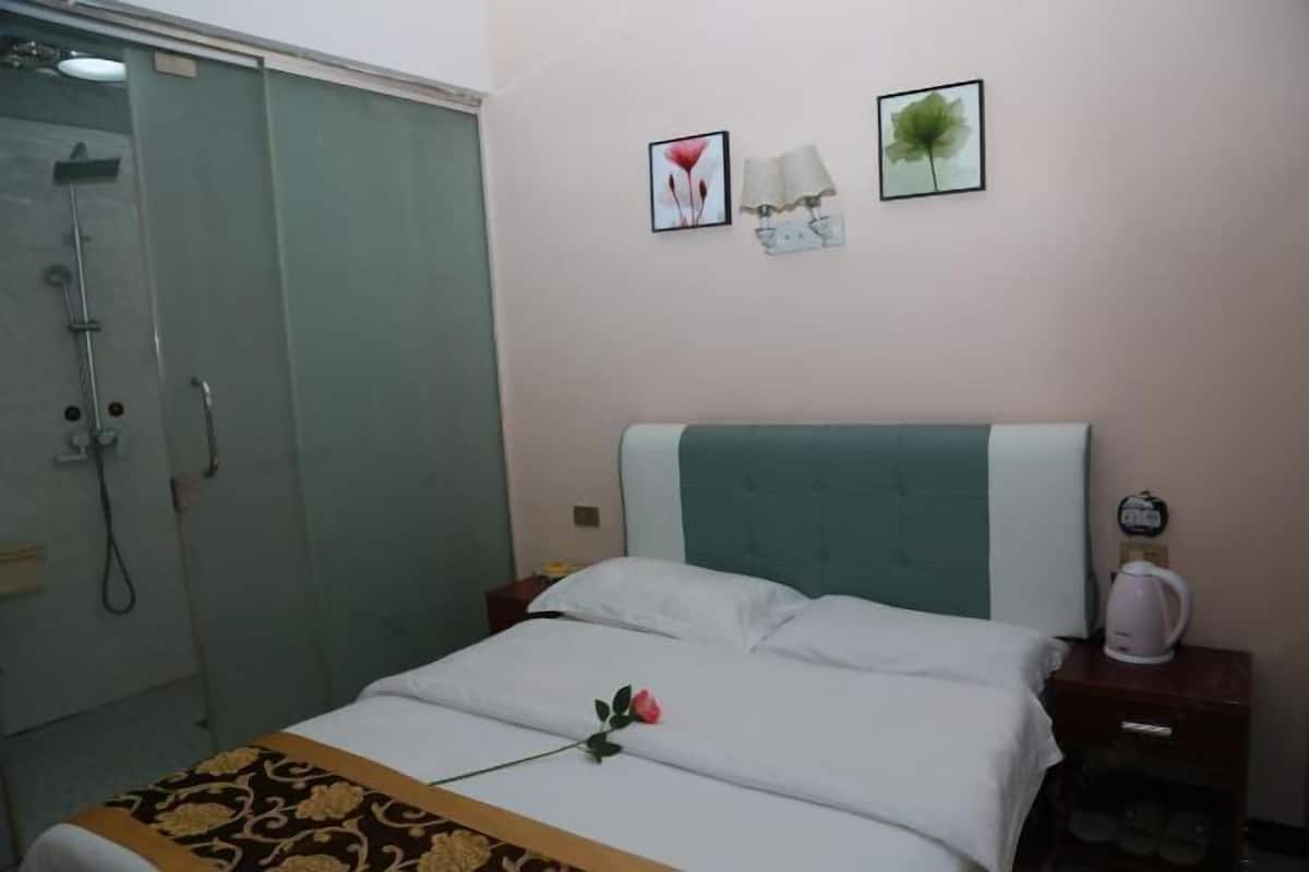Habitación de hotel con cama, mesita de noche y ducha. En la pared, dos cuadros enmarcados.