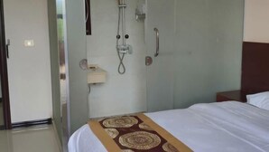 A hotel room with a bed, a glass-enclosed shower, a bedside table, and a nightstand. - Pingtang Yuqi Hotel (Pingtang)