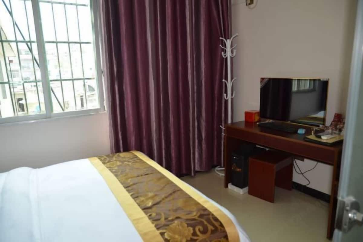 Habitación de hotel con cama, escritorio con computadora, televisor y ventana con cortinas.