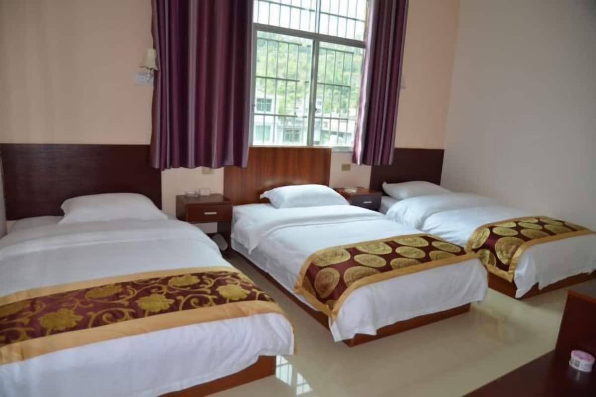 Una habitación de hotel con tres camas, una ventana con cortinas y un cabecero de madera.