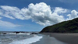 En strand med vågor, en klar himmel och en kulle med växtlighet.