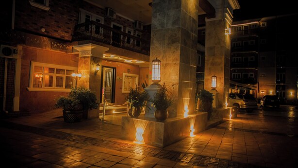 A nighttime view of a hotel lobby with a central fountain, potted plants, and a well-lit entrance.