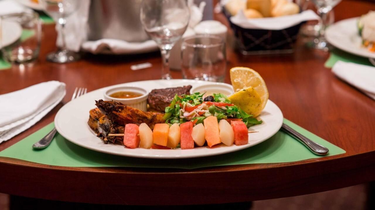 Un plato de comida con brochetas, ensalada y un gajo de limón sobre una mesa.