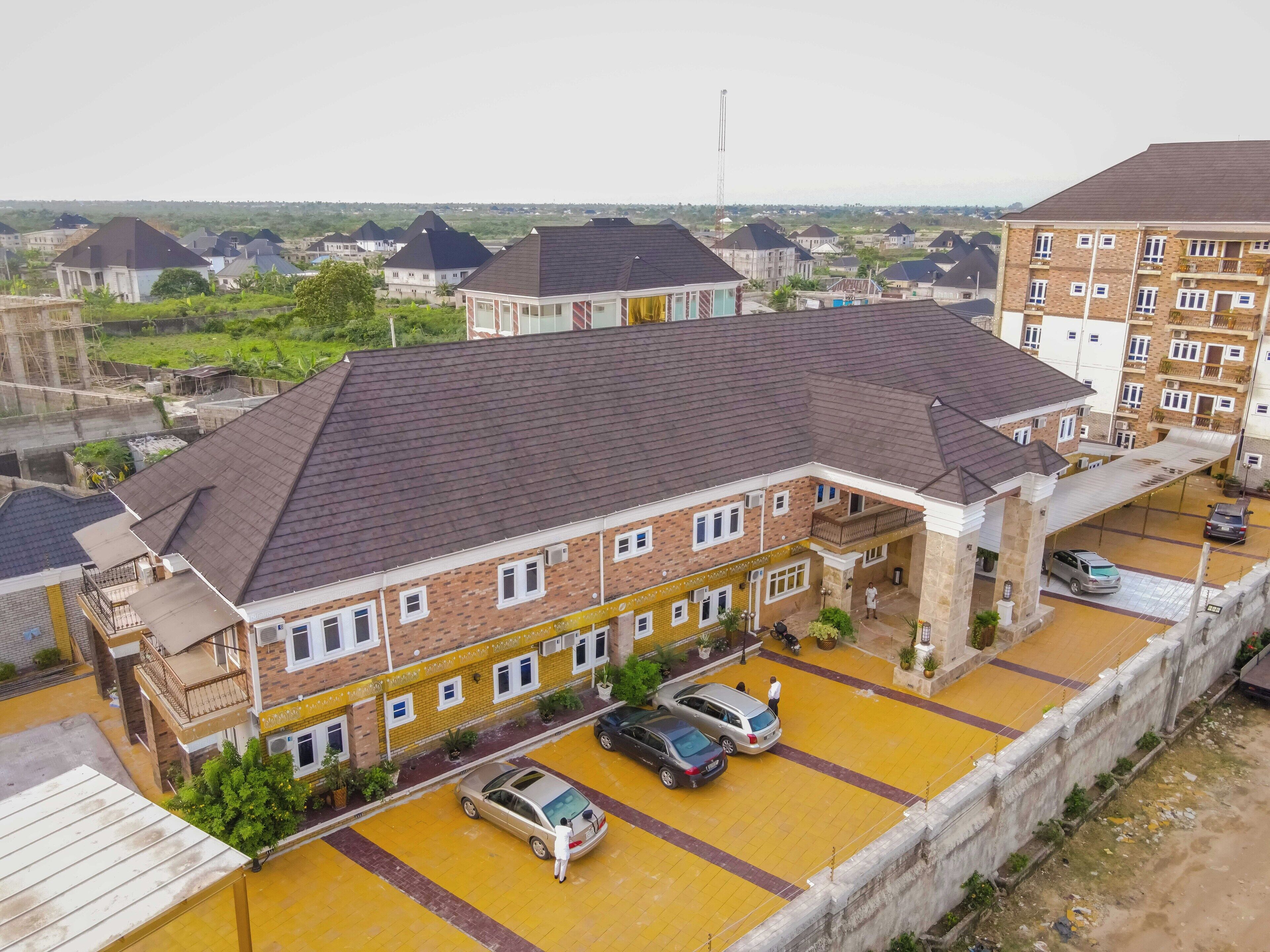 A multi-story residential building with a brick facade, a flat roof, and a parking area with yellow paving.