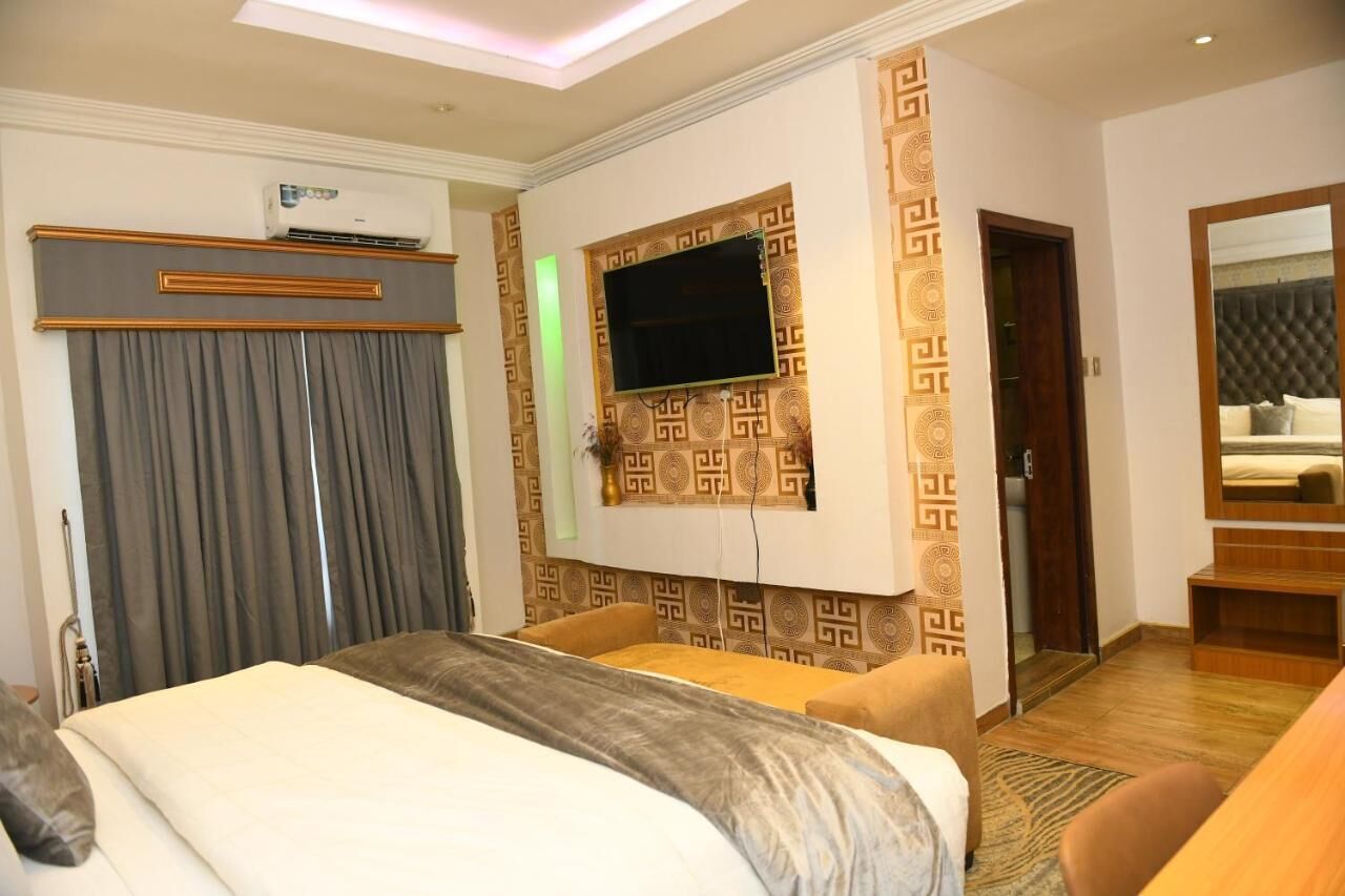 A hotel room with a bed, a TV mounted on the wall, a wardrobe, and a mirror.