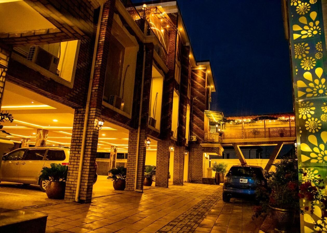 A multi-story building with a brick facade, multiple balconies, and a covered entrance area with potted plants.