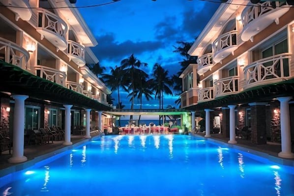Una piscina de hotel con vistas a palmeras y la fachada de un edificio con balcones.