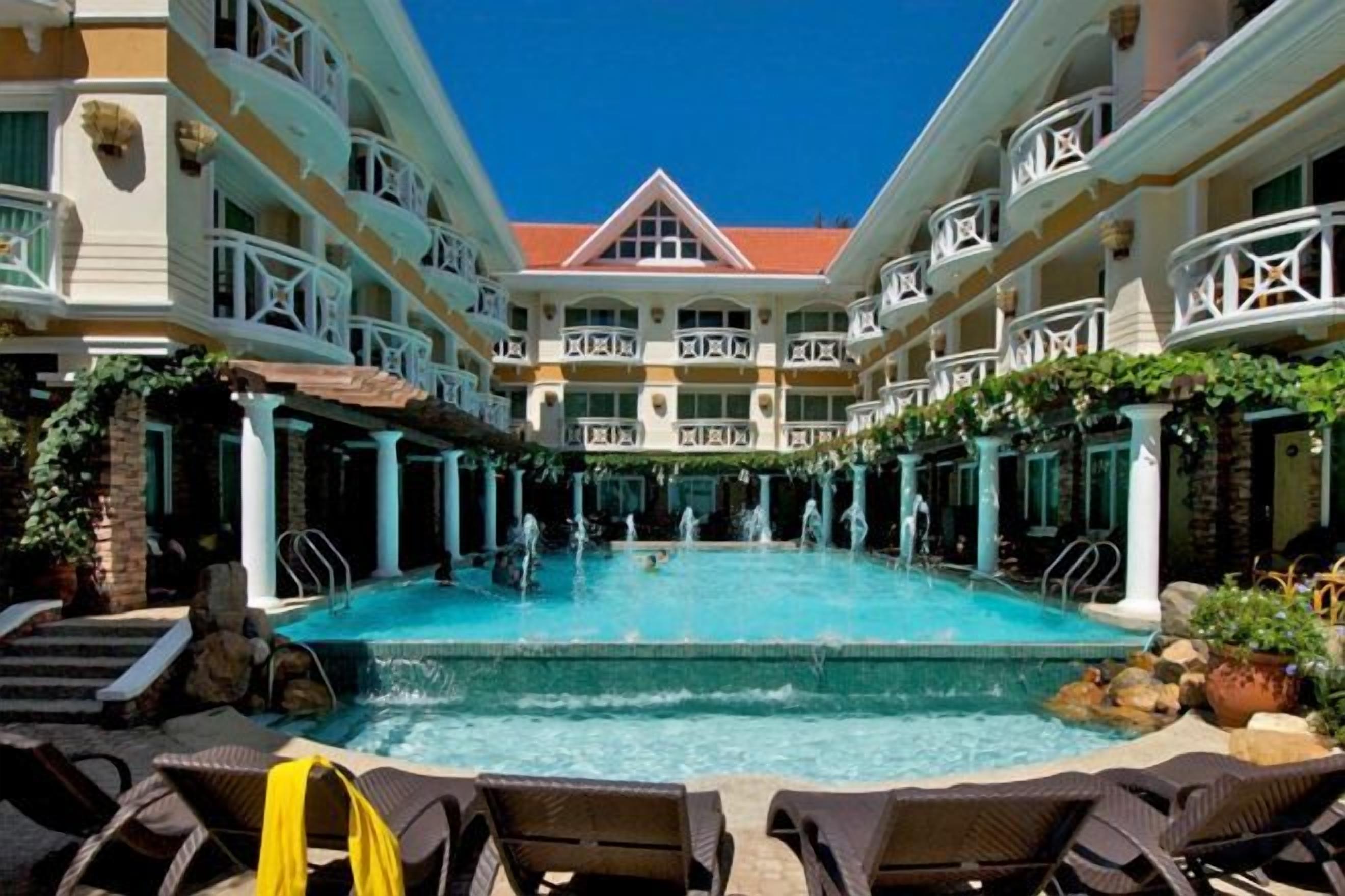 Un espace piscine d’hôtel doté de plusieurs niveaux de balcons, d’une piscine centrale et de chaises longues.