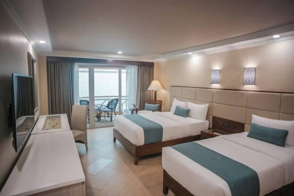 Habitació d'hotel amb dos llits, un escriptori, una cadira i un balcó.