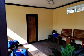 Una habitación con una puerta de madera, dos bancos de madera, una mesa azul con una silla y una planta en maceta.