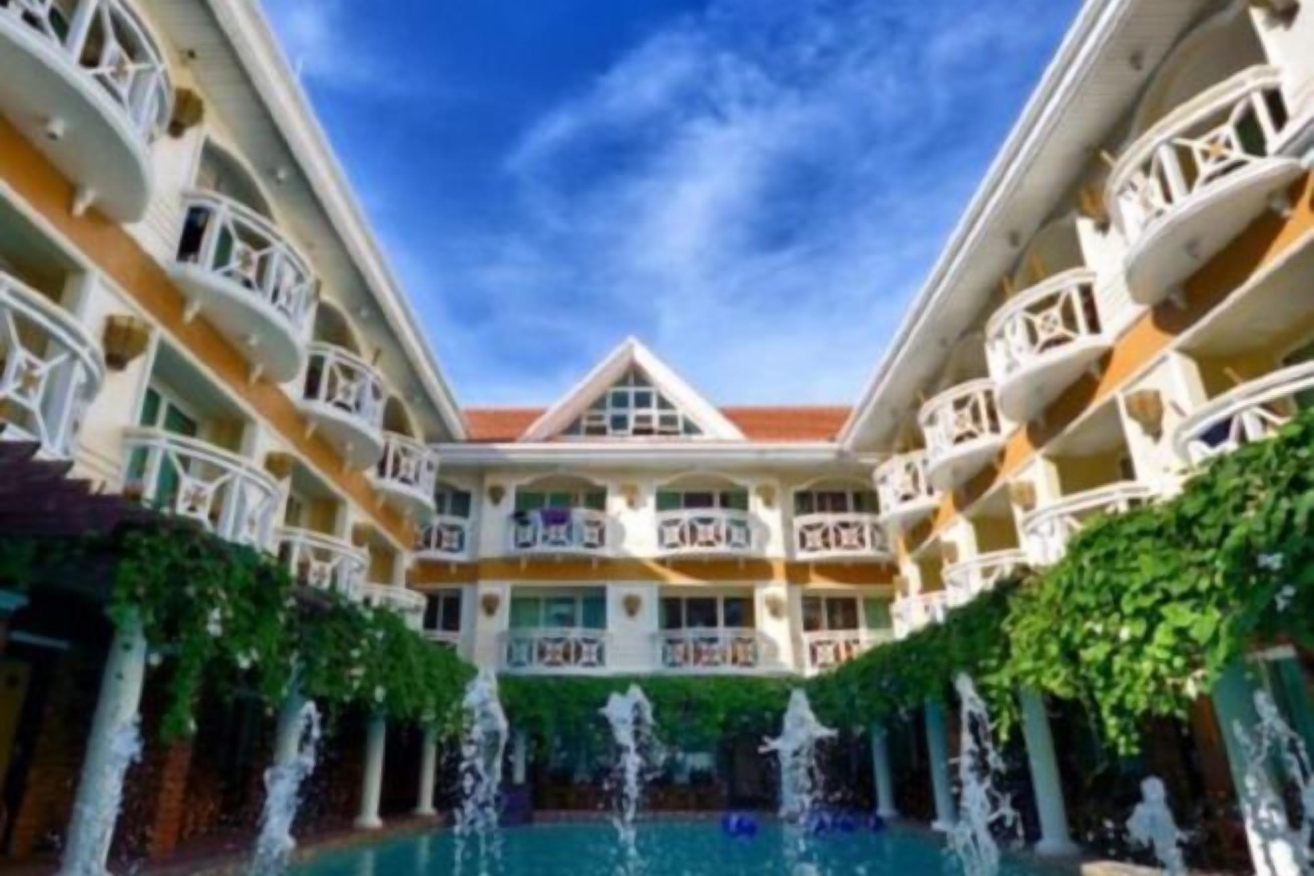 Un hotel con varios balcones, un patio central con una fuente y una piscina.