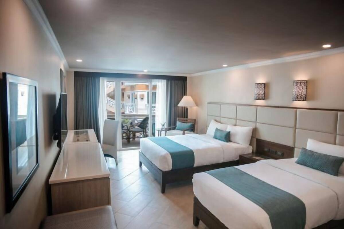 Habitació d'hotel amb dos llits, escriptori, televisió i un balcó amb mobiliari exterior.