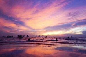 Una playa con barcos y gente al atardecer.