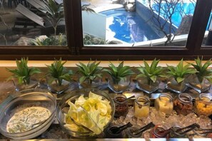 Un bufé con diferentes opciones de comida, incluyendo un tazón de ensalada, frascos de salsas y pequeñas plantas en macetas.