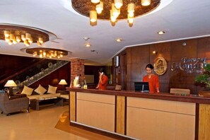 Un hall d’hôtel comprenant un comptoir d’accueil, un escalier et un espace détente.