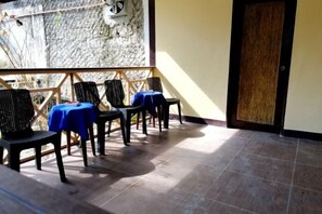 Un balcón con sillas y mesas, un muro de piedra y una puerta de madera.