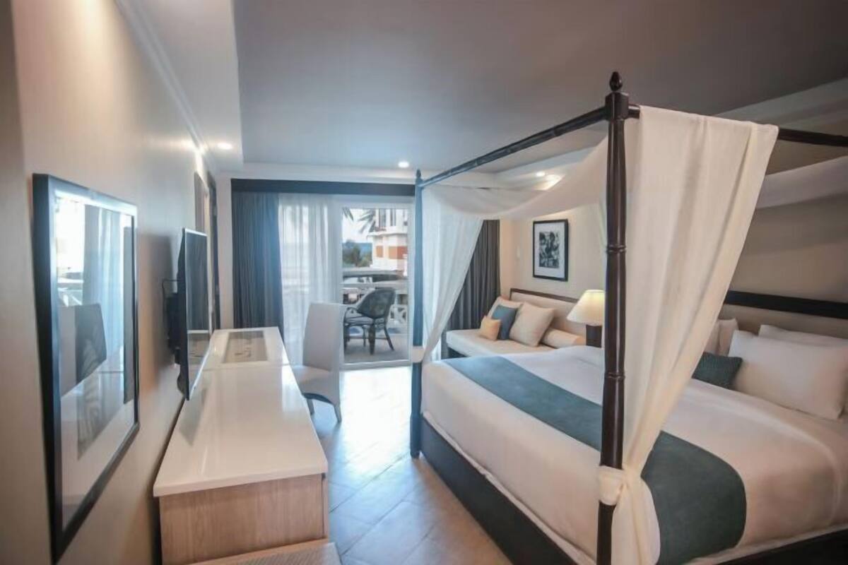 Habitació d'hotel amb un llit amb cortines i pilars, un escriptori i una cadira.