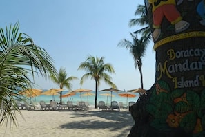 Una playa con palmeras, sillas de playa y sombrillas.