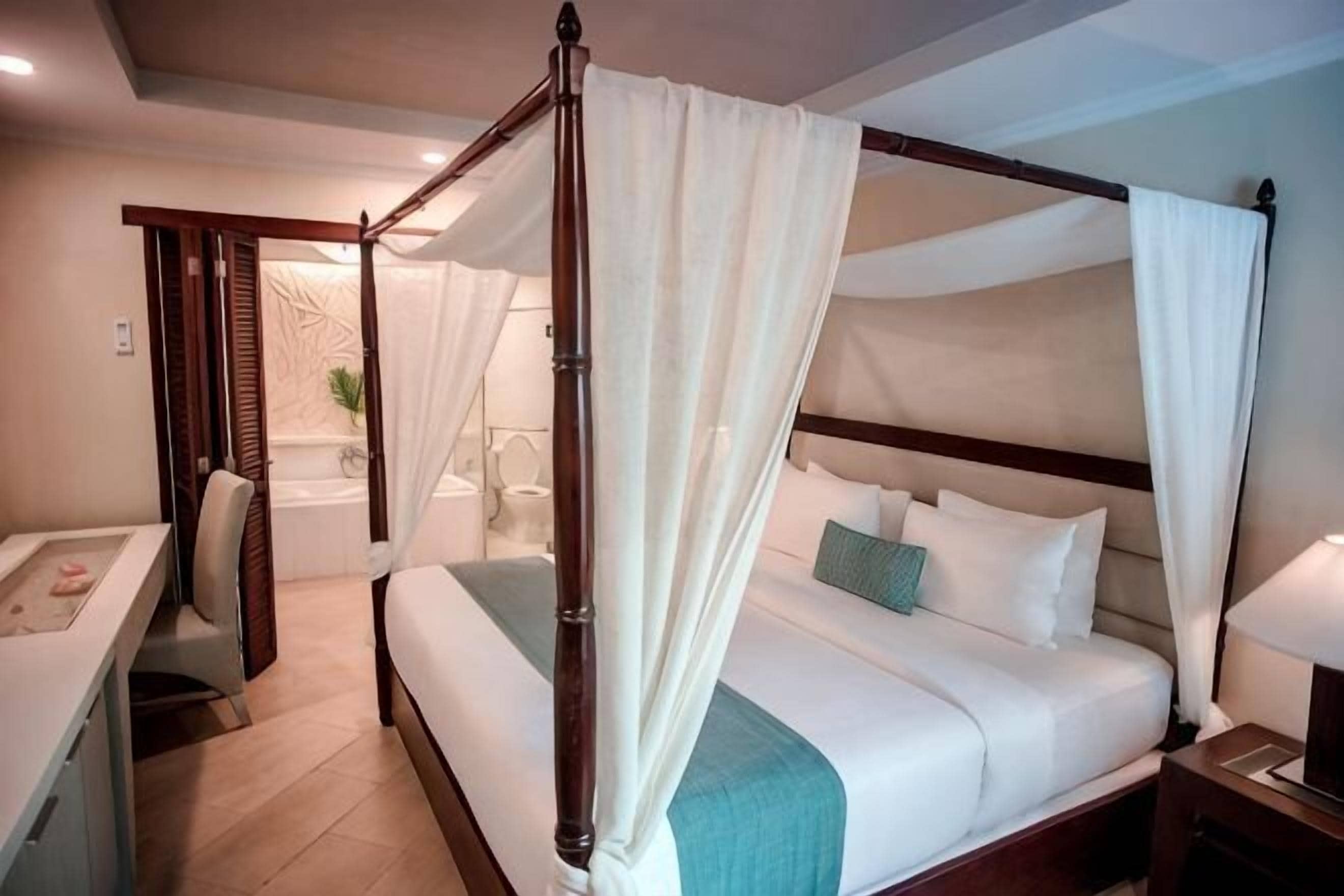 A four-poster bed with a canopy, a bedside table, a nightstand, and a view of a bathroom.