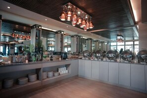 Un área de bar moderna con una barra larga, iluminación colgante y vista de la cocina al fondo.