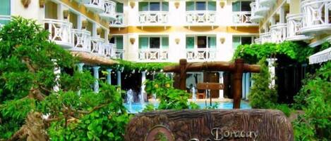 A resort with a central water feature, lush greenery, and a sign indicating a tropical garden theme.