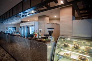 Un hall d’hôtel avec un comptoir d’accueil en marbre, une vitrine en verre où sont présentés des desserts et un lustre.