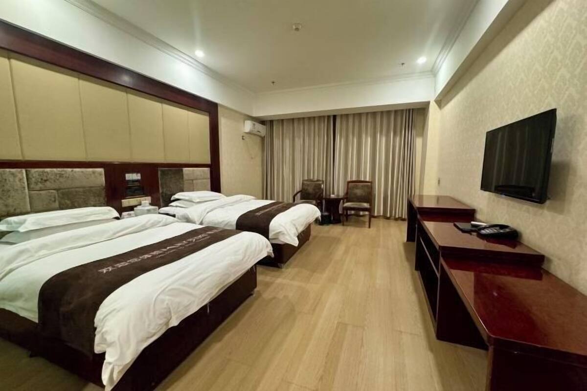 A hotel room with two beds, a desk, a chair, a TV, and a curtain.